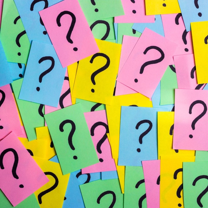 A colorful pile of sticky notes, each hand-drawn with a large question mark, in pink, blue, green, and yellow